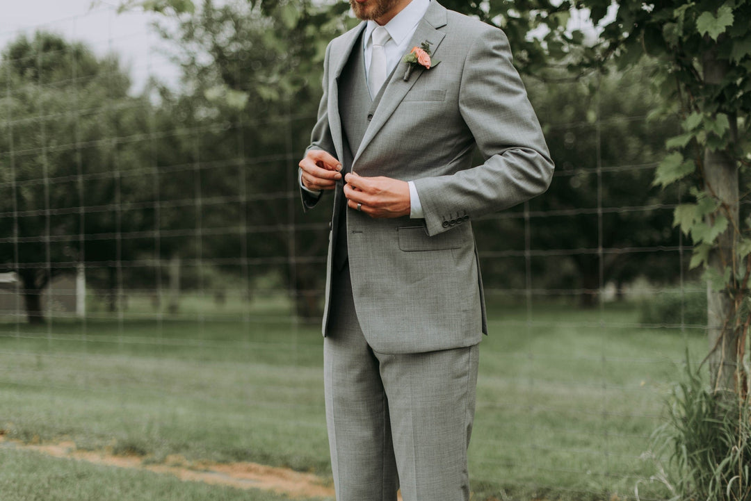 groom adjusting tie while wearing a wedding suit from Karako Suits