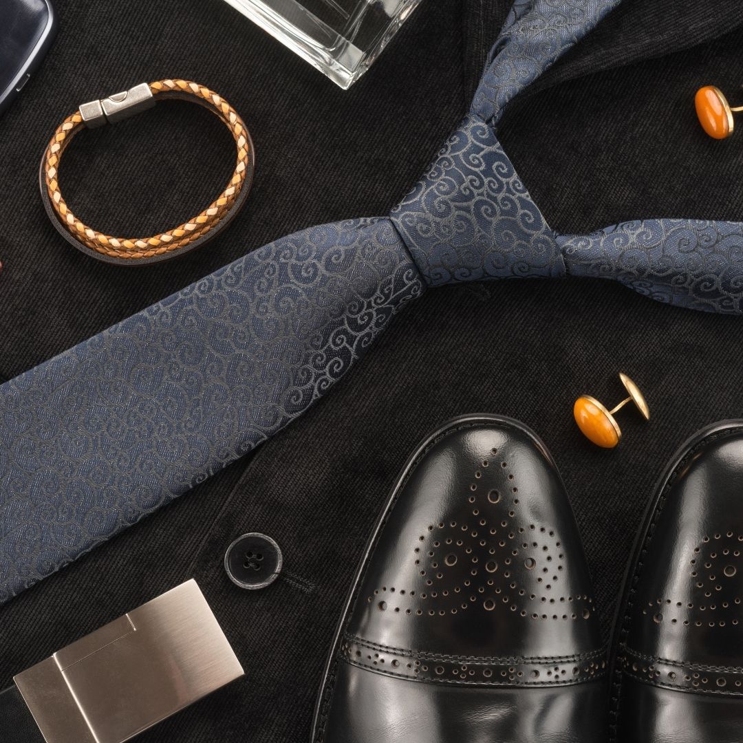 Several men's accessories displayed: black dress shoes, blue necktie, leather bracelet, cufflinks, cologne bottle, and a metallic clip.