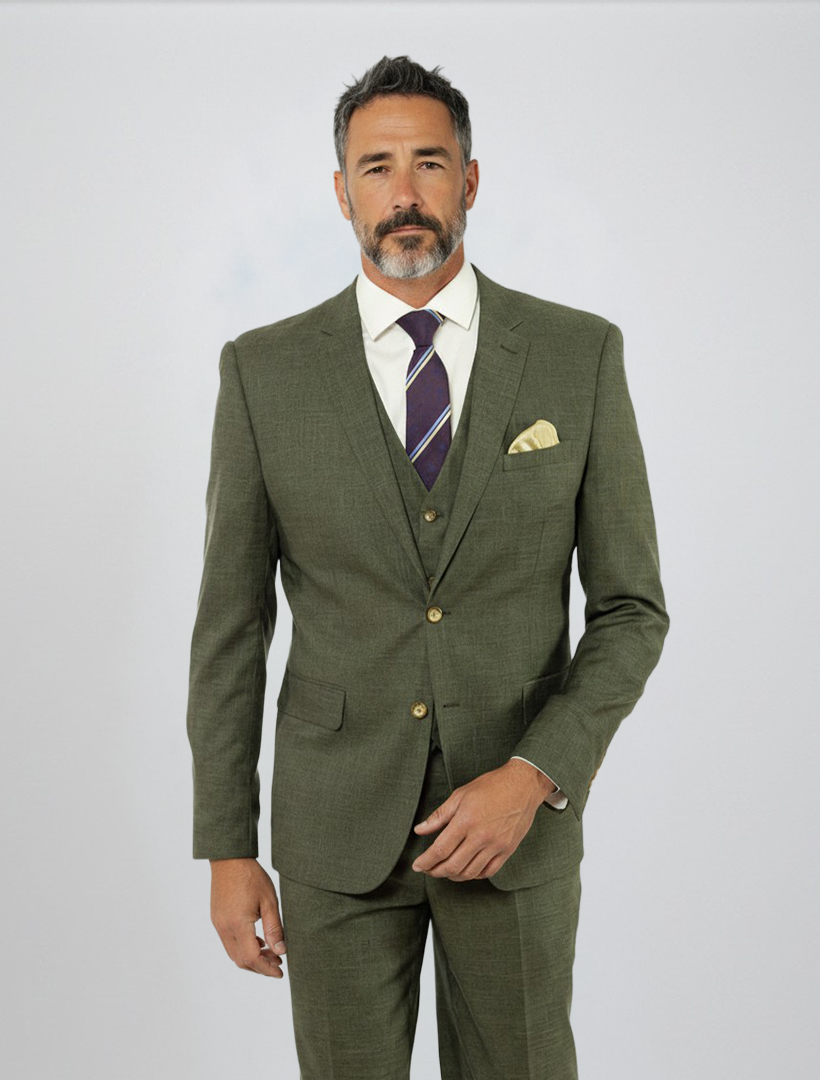 A man stands against a plain light background dressed in the FUBU Olive Green Solid Vested Suit by Fubu The Colle, paired with a white shirt, striped tie, and yellow pocket square.