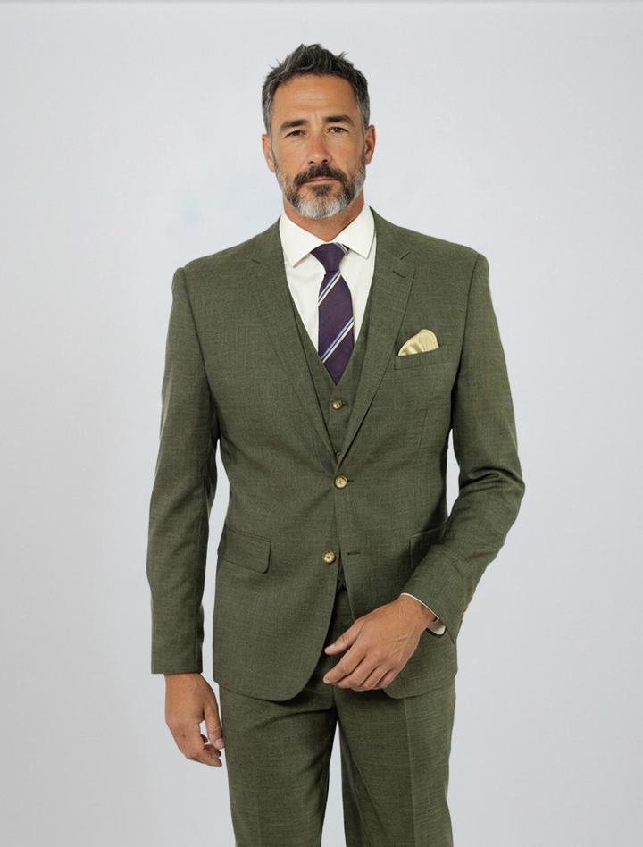 A man stands against a plain light background dressed in the FUBU Olive Green Solid Vested Suit by Fubu The Colle, paired with a white shirt, striped tie, and yellow pocket square.