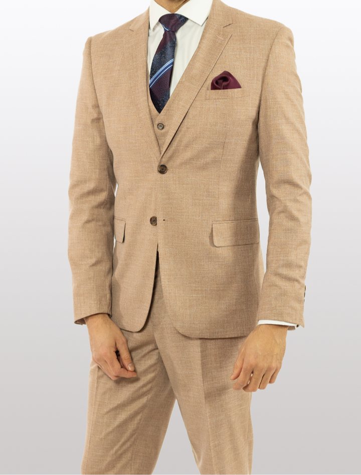 A person wearing a FUBU Dusty Pink Solid Vested Suit from Fubu The Colle, complete with a dark tie and maroon pocket square, with stretch armhole details, stands against a plain background.