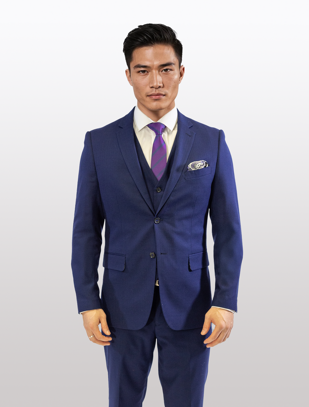 A man wearing a FUBU Berry Blue Vested Suit by Fubu The Colle, paired with a white shirt and purple striped tie, stands against a plain background.