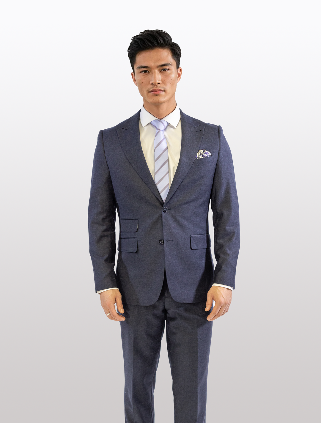 A person in a FUBU Polo Blue Peak Lapel 2-Piece Suit by Fubu The Colle, wearing a light shirt and striped tie, stands against a plain white background.