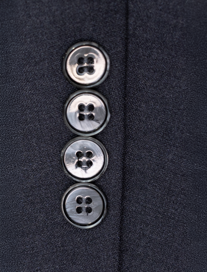 Close-up of four silver buttons in a vertical line on the dark fabric of the FUBU Polo Blue Peak Lapel 2-Piece Suit by Fubu The Colle.