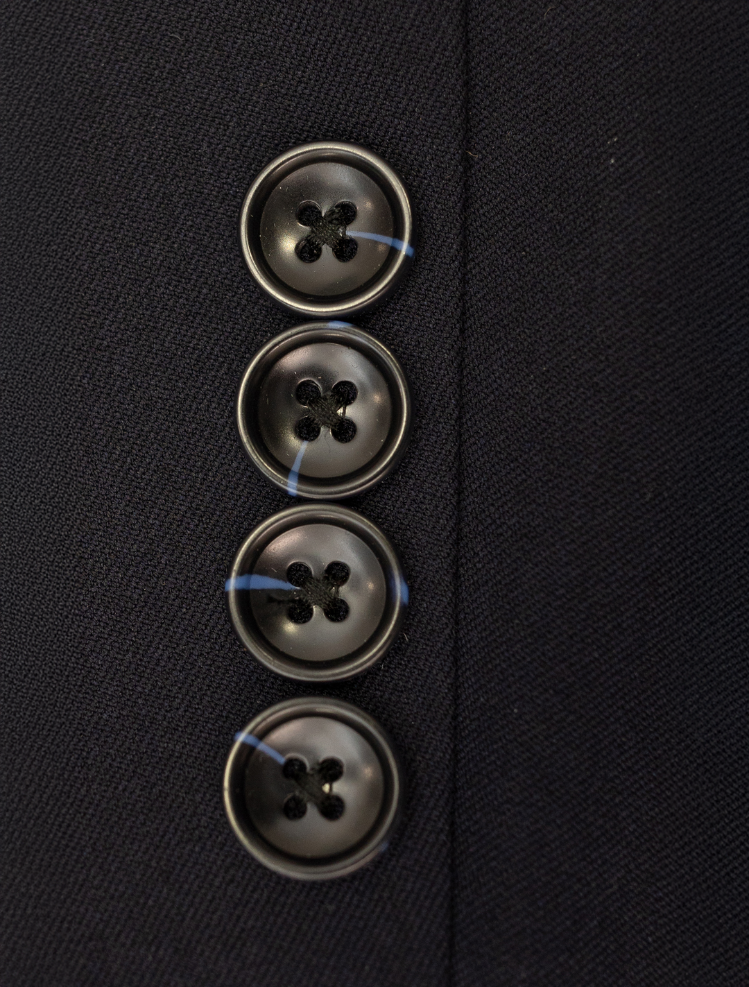 Close-up of four black buttons sewn vertically on dark fabric, characteristic of the FUBU Midnight Navy with Debossed Windowpane Vested Suit by Fubu The Colle.