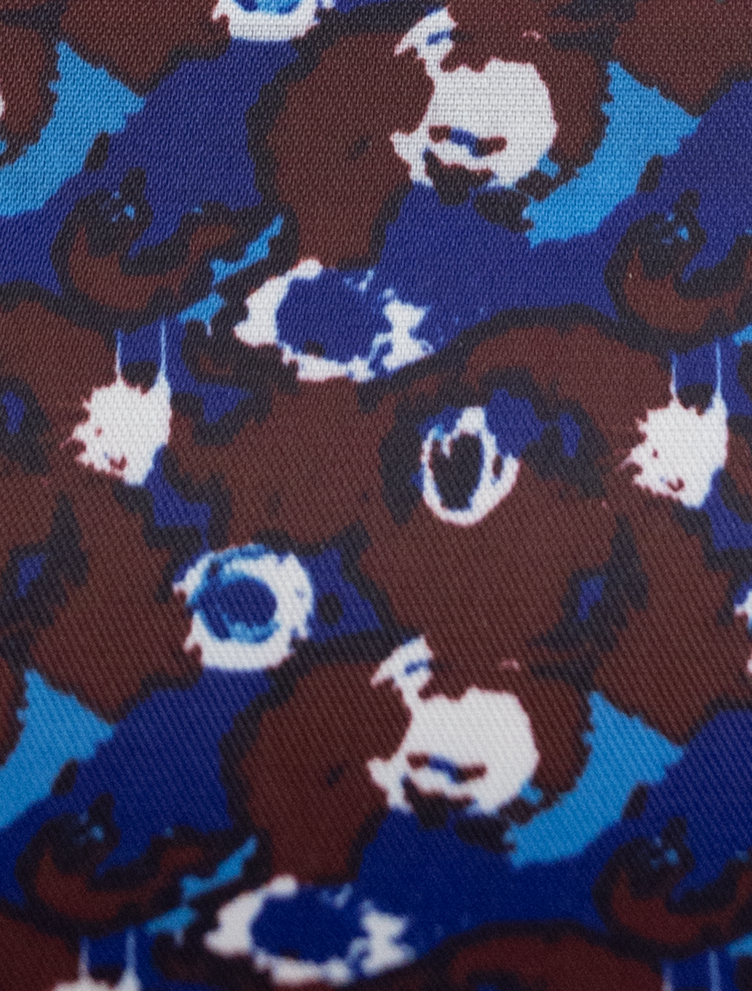 A modern suit design, the FUBU Midnight Navy with Debossed Windowpane Vested Suit by Fubu The Colle showcases abstract patterns in brown, blue, and white on a textured surface.