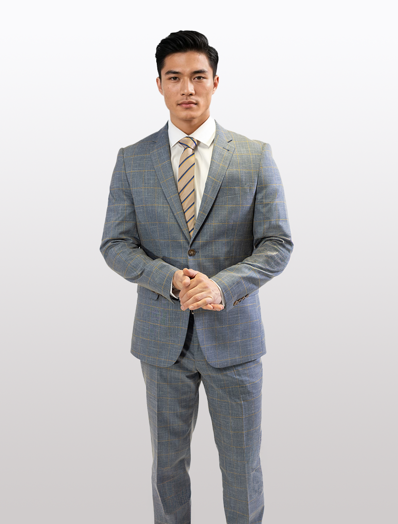 A man in a FUBU Steel Blue with Mustard Windowpane 2-Piece Suit from Fubu The Colle stands against a plain backdrop, highlighting the slim fit design with his hands together.