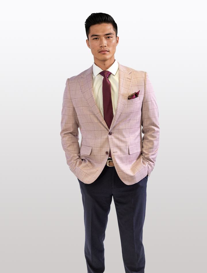 A person stands confidently in a FUBU Rose with Cherry Windowpane Sport Jacket from Fubu The Colle, paired with a white shirt, burgundy tie, and dark pants, hands in pockets against a plain background.