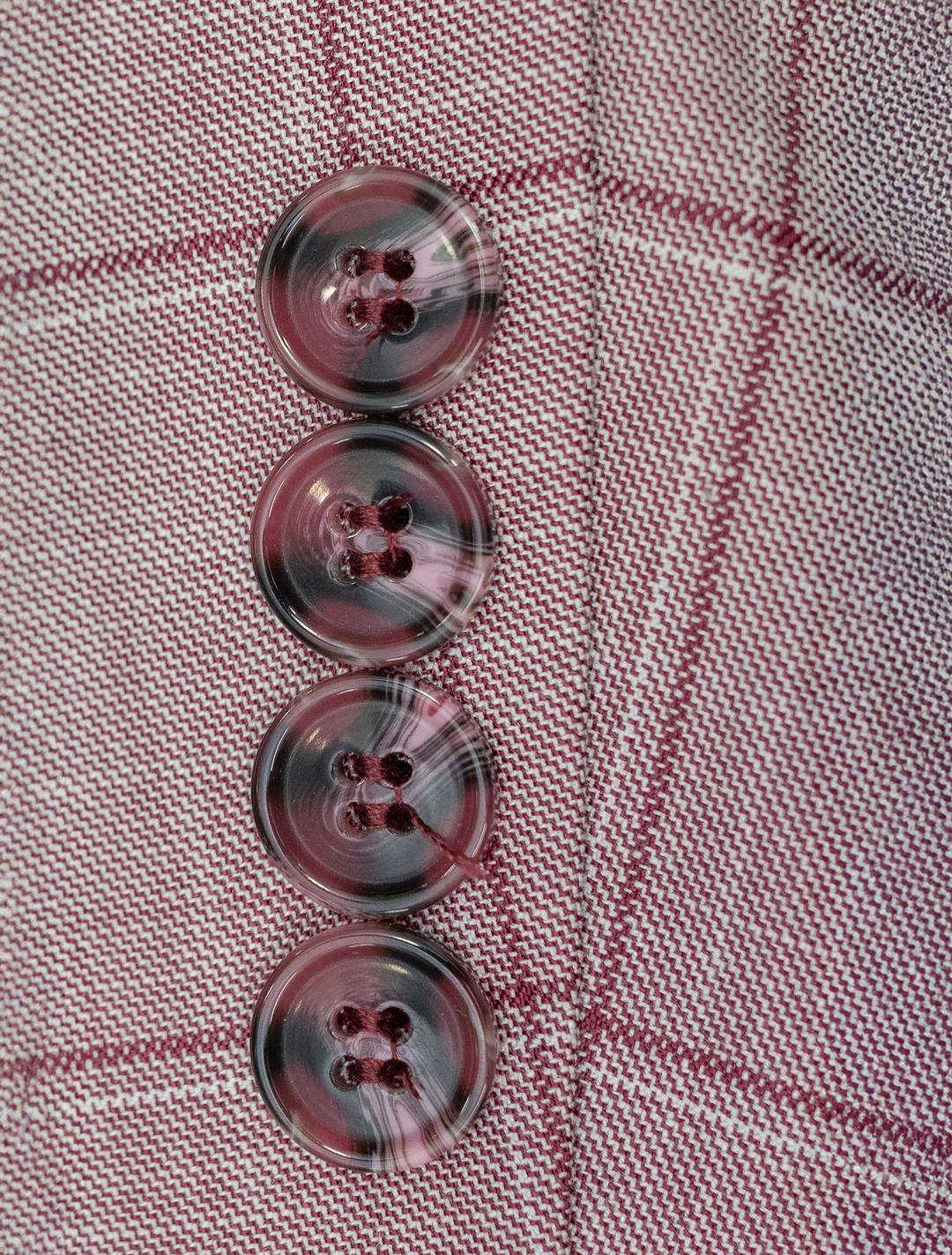 A close-up of four marbled buttons on red plaid fabric, arranged vertically, evokes the unique detailing of the FUBU Rose with Cherry Windowpane Sport Jacket by Fubu The Colle.