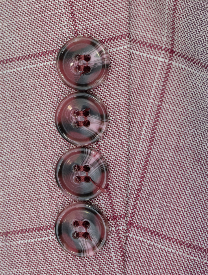 A close-up of four marbled buttons on red plaid fabric, arranged vertically, evokes the unique detailing of the FUBU Rose with Cherry Windowpane Sport Jacket by Fubu The Colle.