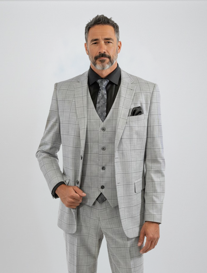 A man with short gray hair and a beard wears the FUBU Light Grey with Charcoal Windowpane Vested Suit by Fubu The Colle, paired with a black shirt and patterned tie, standing against a plain white background.