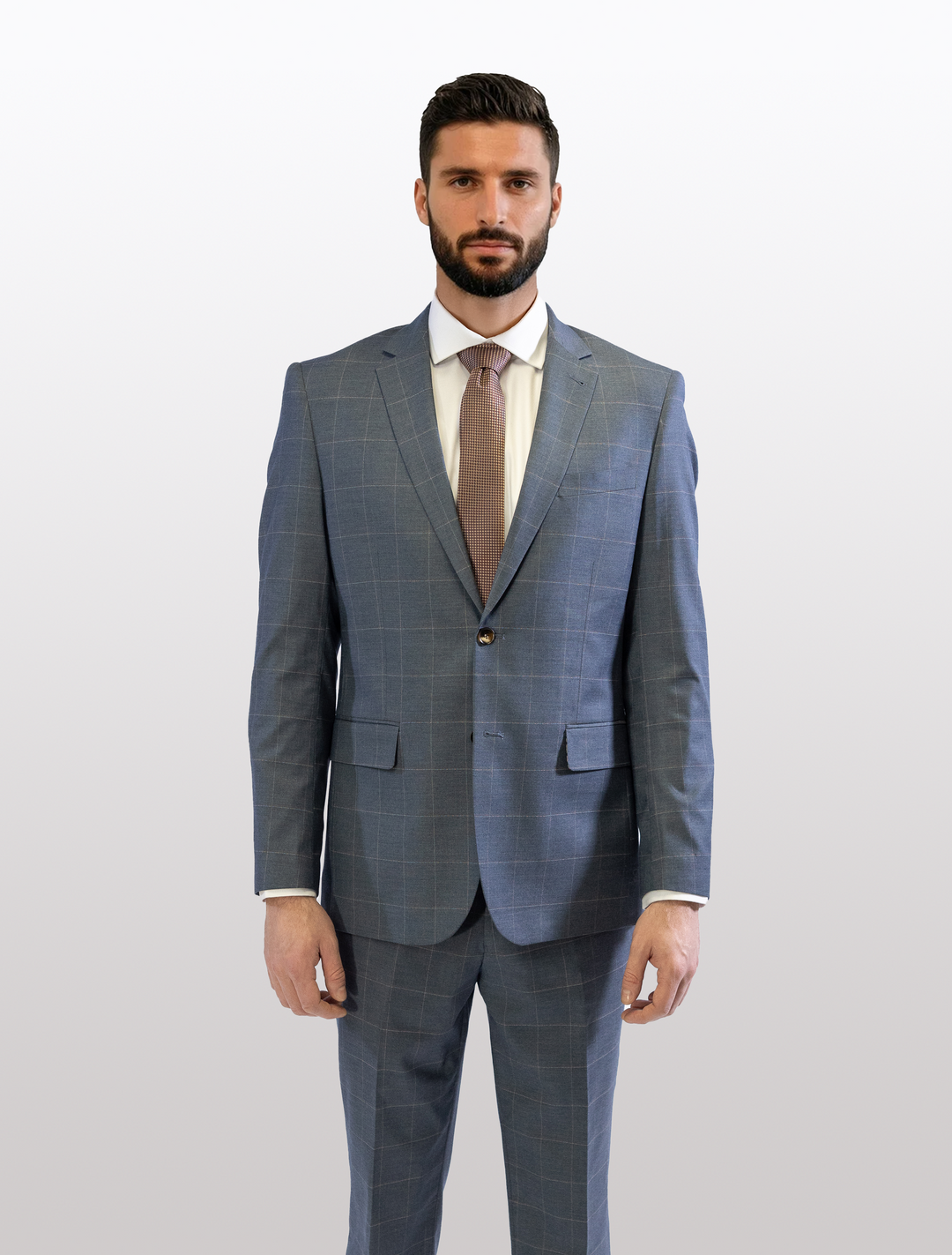 A bearded man is wearing a FUBU Gravel Blue with Peach Windowpane 2-Piece Suit from Fubu The Colle, paired with a white shirt and brown tie, standing against a simple light background.