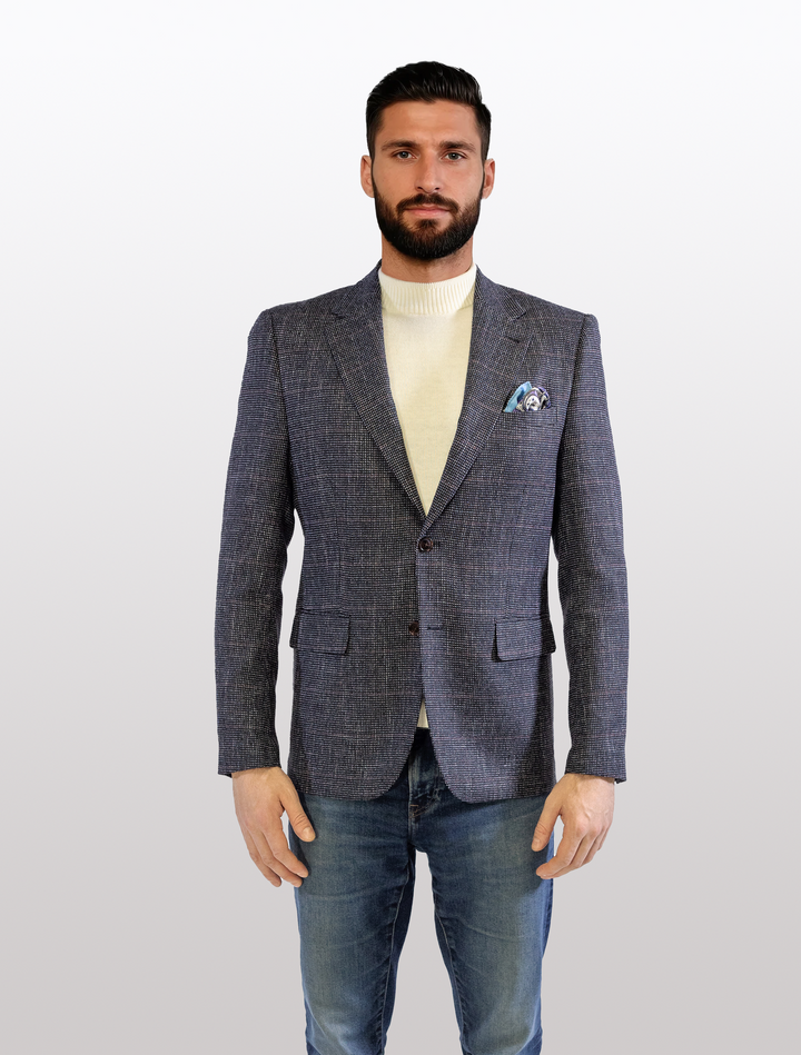 A bearded man wore a FUBU Textured Navy with Brick Windowpane Sport Jacket from Fubu The Colle, paired with a white turtleneck and jeans, standing against a plain background.