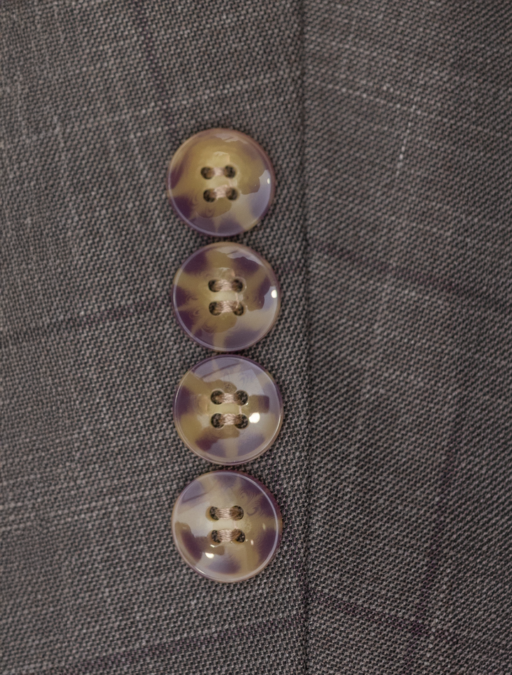Close-up of four marbled buttons on a dark checkered fabric, reminiscent of a modern fit suit, sewn vertically on the FUBU Taupe with Brown Windowpane Vested Suit by Fubu The Colle.
