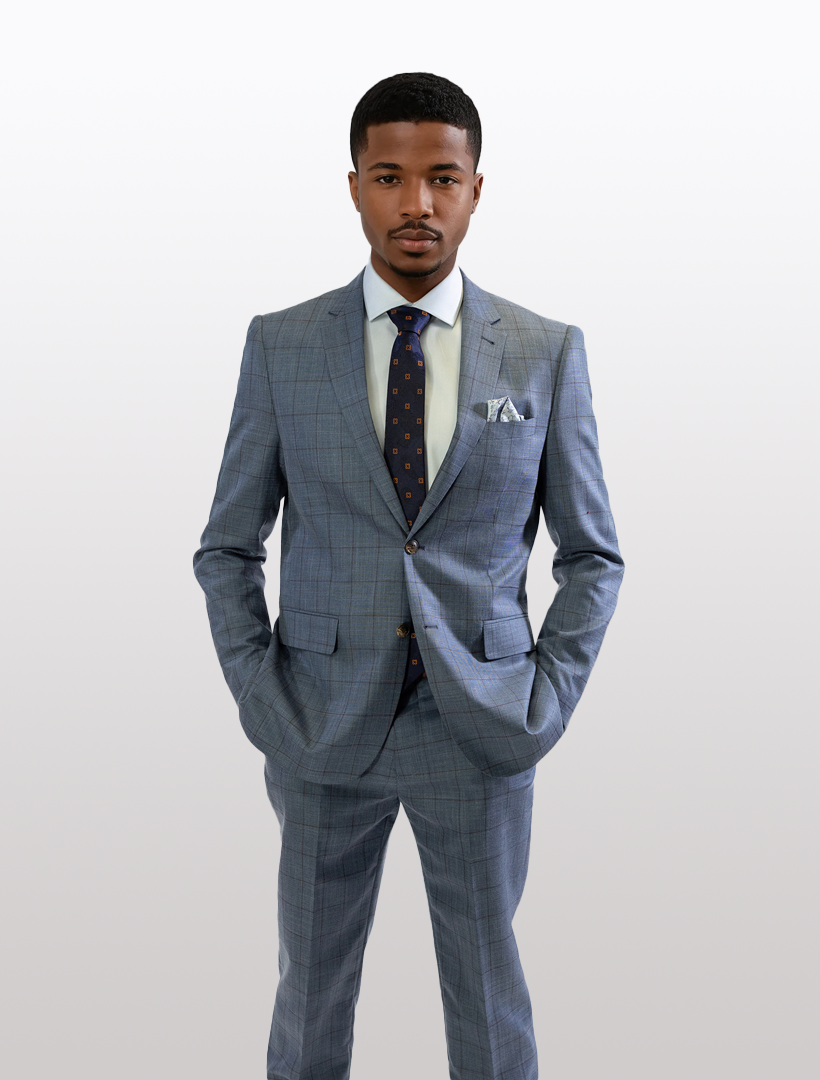 A man in a FUBU Denim Blue with Rust Windowpane 2-Piece Suit from Fubu The Colle stands against a plain background, hands in pockets, wearing a white shirt, dark tie, and pocket square.