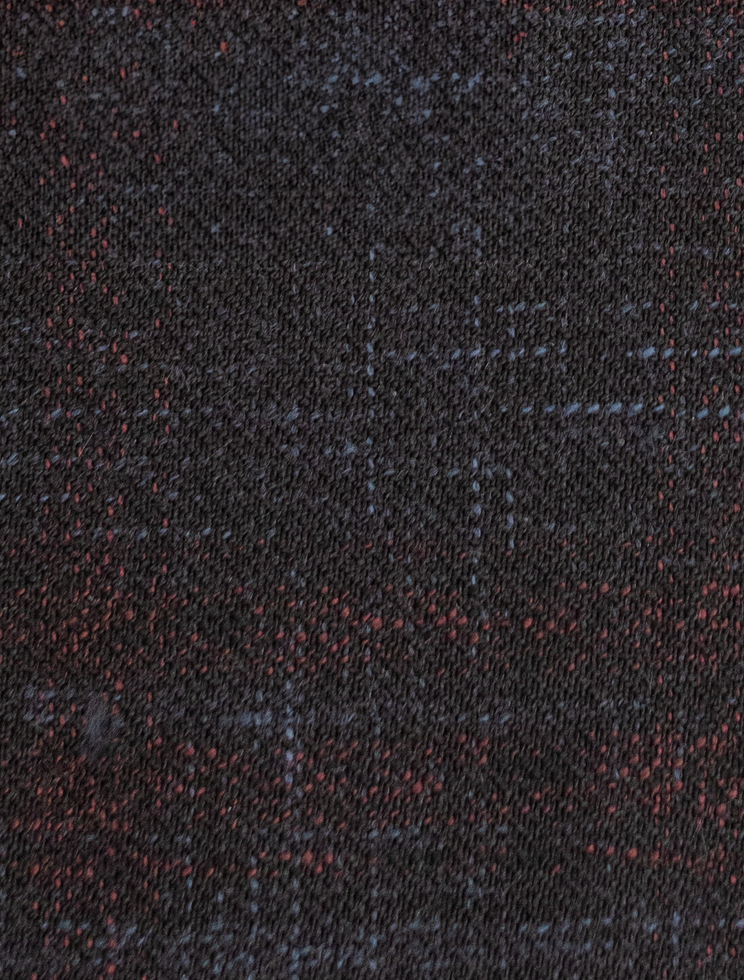 A close-up of the FUBU Midnight Navy with Wine Windowpane Sport Jacket from Fubu The Colle showcases a dark textured fabric with subtle red and blue specks, echoing the elegance typical of slim fit sport coats.