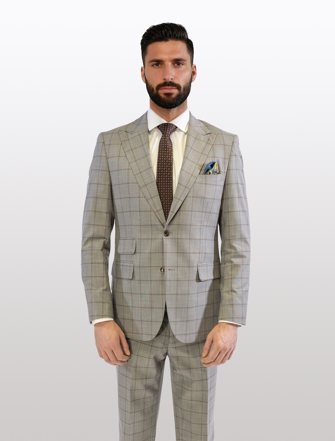 A man stands against a plain background in a slim fit FUBU Oat Grey 2-piece suit with brown windowpane pattern, featuring a peak lapel, expertly crafted from Tetron Rayon by Fubu The Colle.