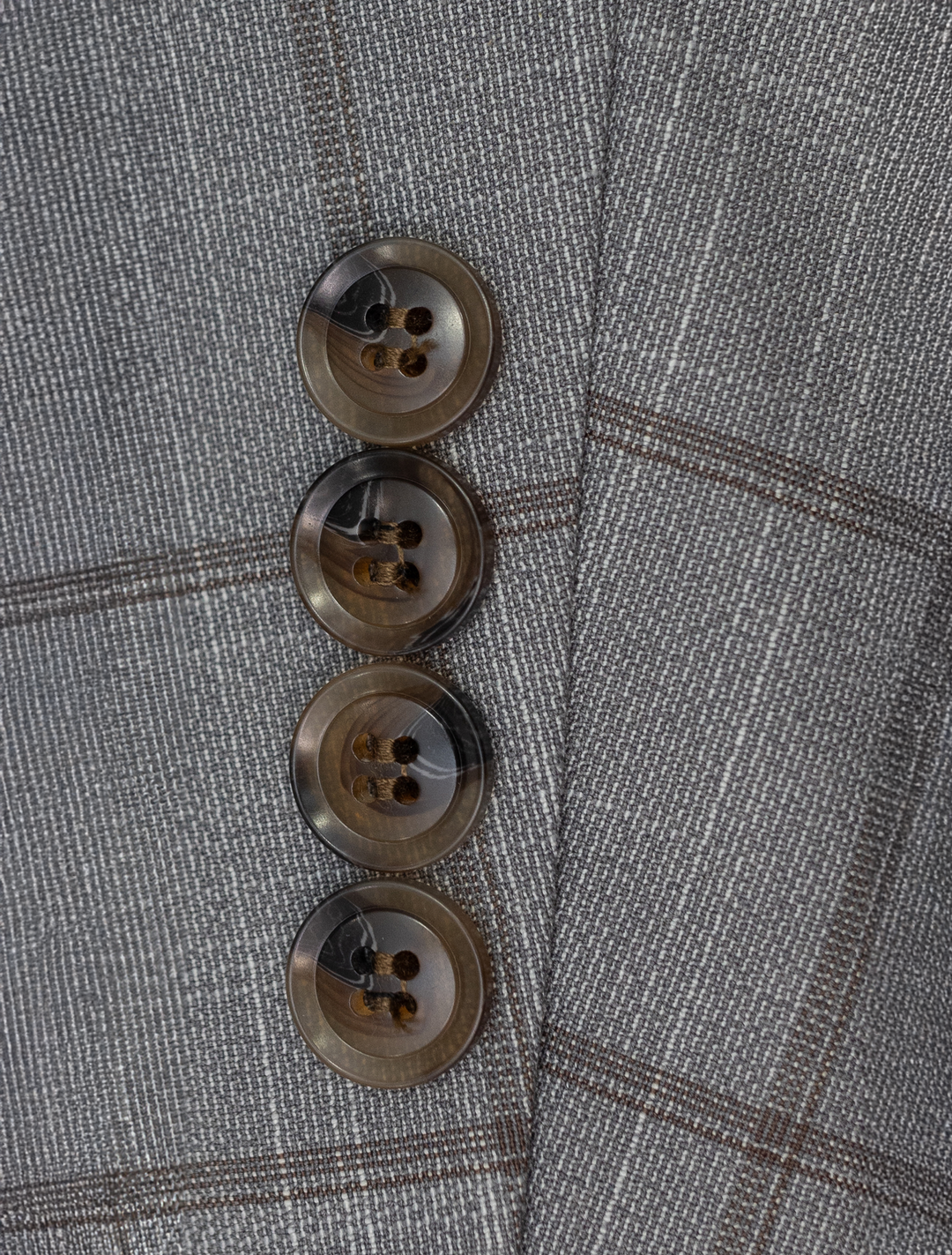 Close-up of the FUBU Oat Grey with Brown Windowpane Peak Lapel 2-Piece Suit sleeve by Fubu The Colle, made from Tetron Rayon, showcasing four vertically aligned brown buttons.