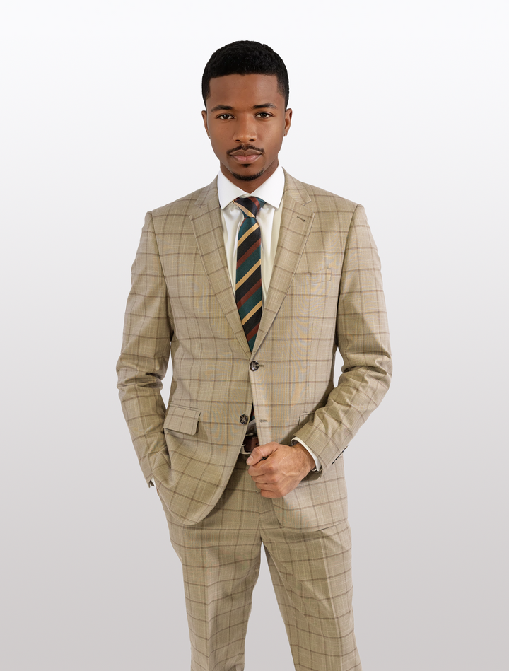 A person in the FUBU Camel with Mocha Windowpane 2-Piece Suit, featuring a modern fit and stretch armholes for added comfort, stands against a plain background, facing forward with one hand in pocket.