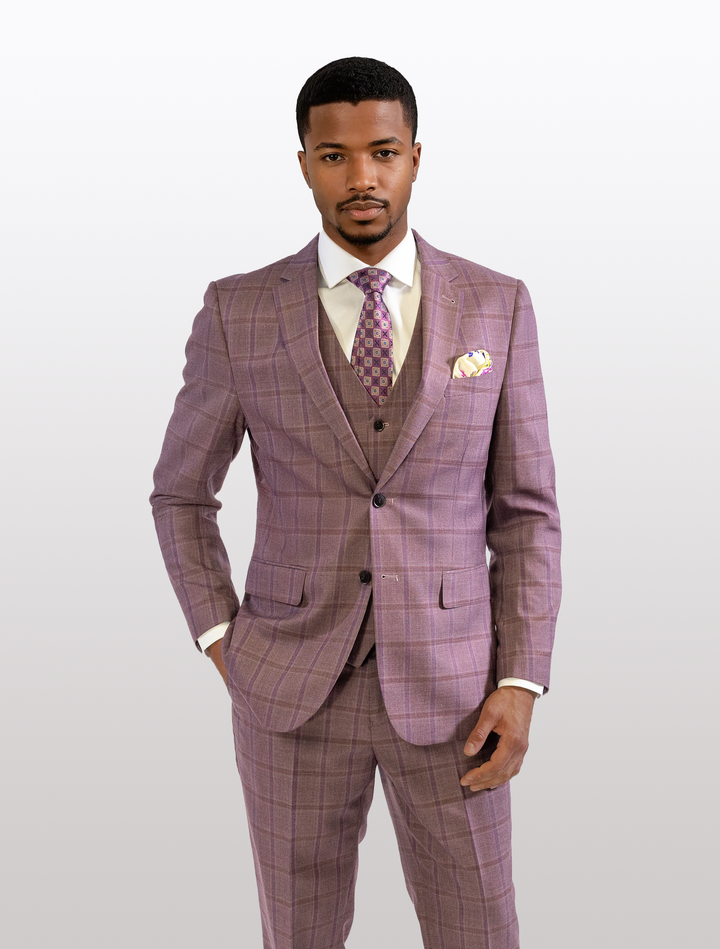 A man stands confidently in a FUBU Mauve Taupe with Purple Windowpane Vested Suit by Fubu The Colle, paired with a matching tie and pocket square, the modern fit accentuating his silhouette against a plain background.