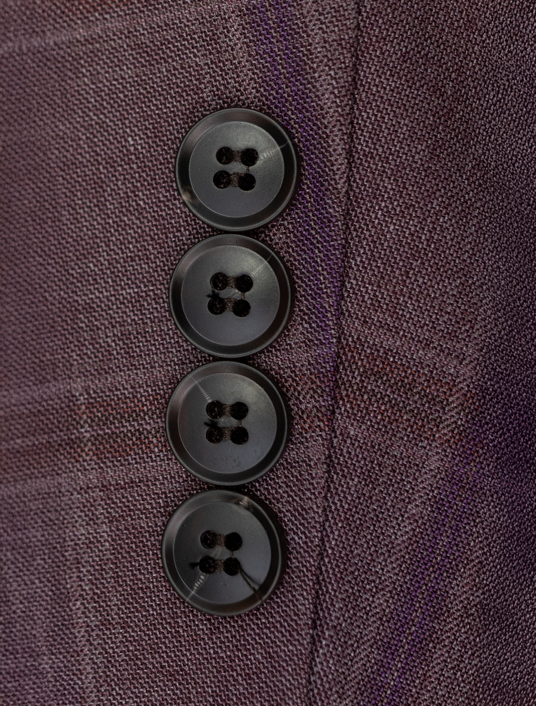 Close-up of four black buttons on mauve taupe fabric with a purple windowpane pattern, resembling the sleek detail of the FUBU Mauve Taupe Vested Suit by Fubu The Colle.