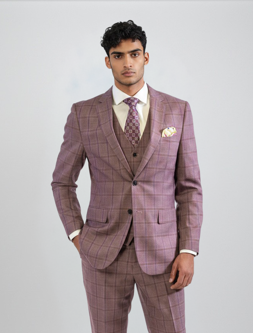 A man wearing the FUBU Mauve Taupe with Purple Windowpane Vested Suit by Fubu The Colle, styled with a patterned tie and pocket square, stands against a plain light gray background. This stylish men’s suit showcases modern details like a stretch armhole for enhanced comfort and ease of movement.