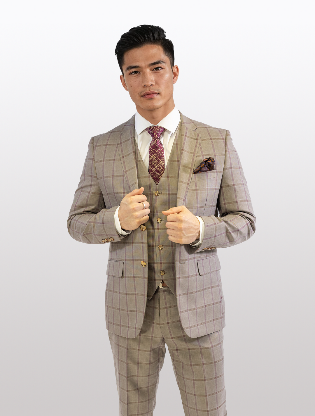 A person models the FUBU Tan with Maroon Windowpane Vested Suit by Fubu The Colle, complete with a red patterned tie, against a white backdrop.