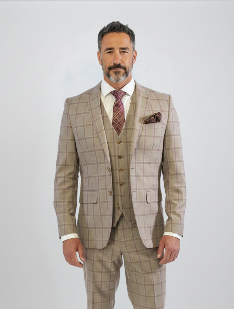 A man wearing the FUBU Tan with Maroon Windowpane Vested Suit by Fubu The Colle, styled with a white shirt and patterned tie, featuring stretch armholes for added comfort, stands against a plain light background.