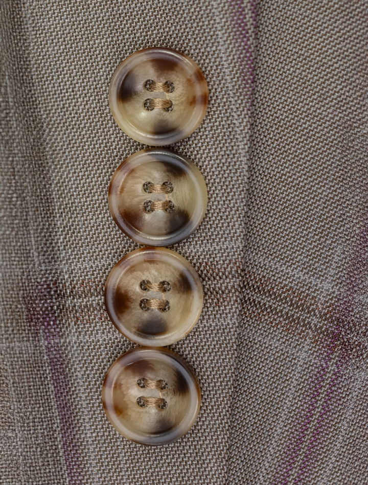 Close-up of four brown horn buttons on the FUBU Tan with Maroon Windowpane Vested Suit by Fubu The Colle, set vertically against a gray plaid fabric.