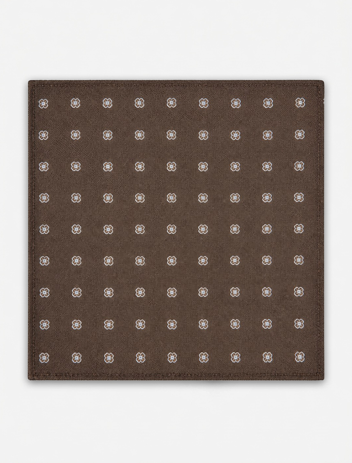 Crafted by Karako Collecti, the Bronze Floral Pocket Square Handkerchief showcases a bronze square microfiber fabric adorned with a grid of small, evenly spaced white and grey floral motifs. Displayed on a plain white background, this stylish men&