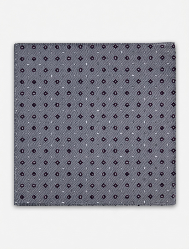 The Karako Collecti Medium Grey with Wine Pocket Square Handkerchief features a refined pattern of small dark purple and white geometric shapes evenly distributed across its gray microfiber fabric, offering an elegant formal accessory suitable for any occasion.