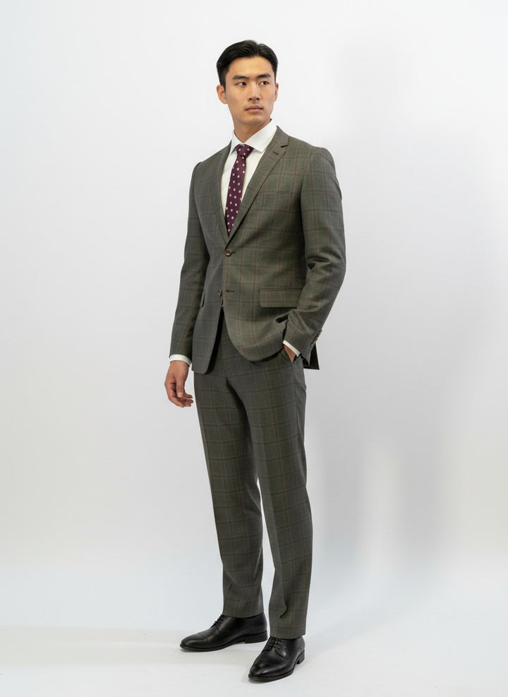 A man is standing in a FUBU Olive with Mahogany Windowpane 2-Piece Suit by Fubu The Colle, paired with a white shirt and maroon polka dot tie against a plain white background.
