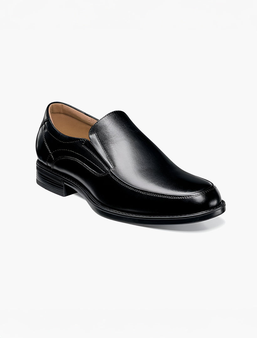 The Florsheim Black Moc Toe Midtown Slip On Shoe features a low heel, rounded toe, subtle stitching, and Comfortech soles. Photographed against a white background.