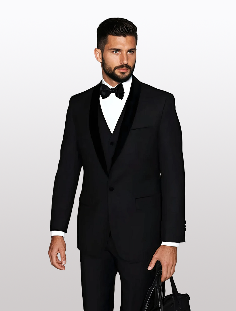 A man in a Statement Men's Black with Black Lapel Vested 100% Wool Velvet Tuxedo, complete with a bow tie, stands against a plain background while holding a black bag.