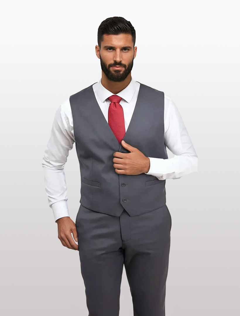 A man in a charcoal grey three-piece suit and a red tie adjusts his slim-fit vest. The Charcoal Grey Men's Slim-Fit Suit Separates Vest by Karako's Suits is crafted from high-performance stretch Tetron Rayon, offering a perfect blend of style and comfort against a plain backdrop.