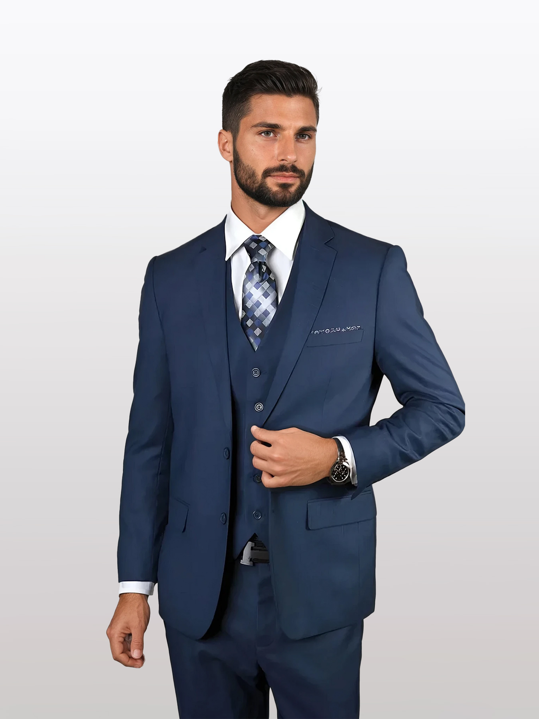 A man in a Statement Men's Sapphire 100% Wool Slim Fit Suit with a patterned tie and white shirt stands against a plain background, touching his lapel with one hand.