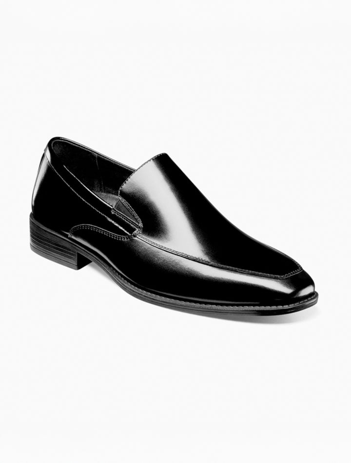 The Stacy Adams Black Aldrich Moc Toe Slip On Shoes feature black leather, a low heel, cushioned insole, and stitching details, shown against a white background.