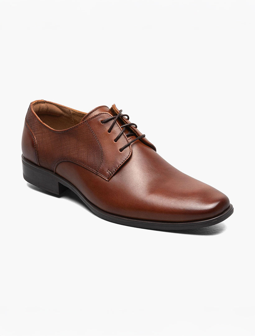 The Florsheim Plain Toe Oxford Cognac Shoe is a brown leather dress shoe with laces, scratch print leather side panels, and a low heel, shown on a plain white background.