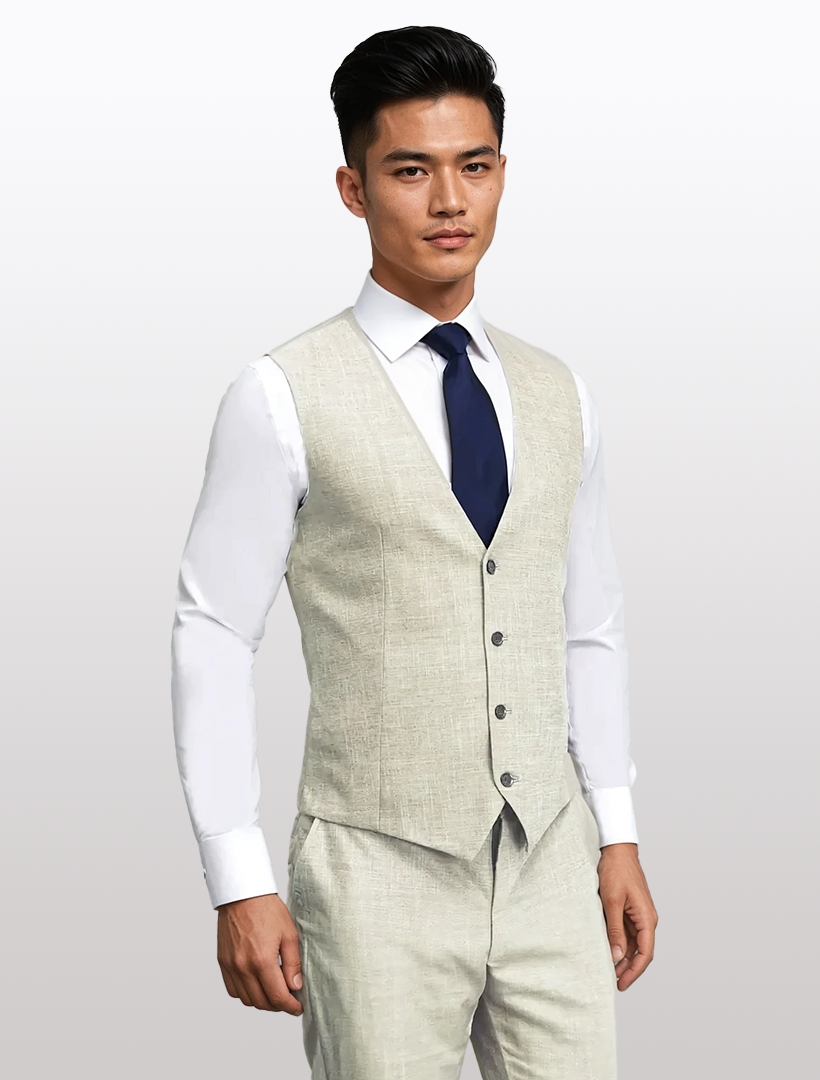 Wearing a Couture 1910 Men's Tan Suit Vest and slim fit beige suit made from high-performance stretch fabric, paired with a white shirt and dark blue tie, a man stands against a light grey background.