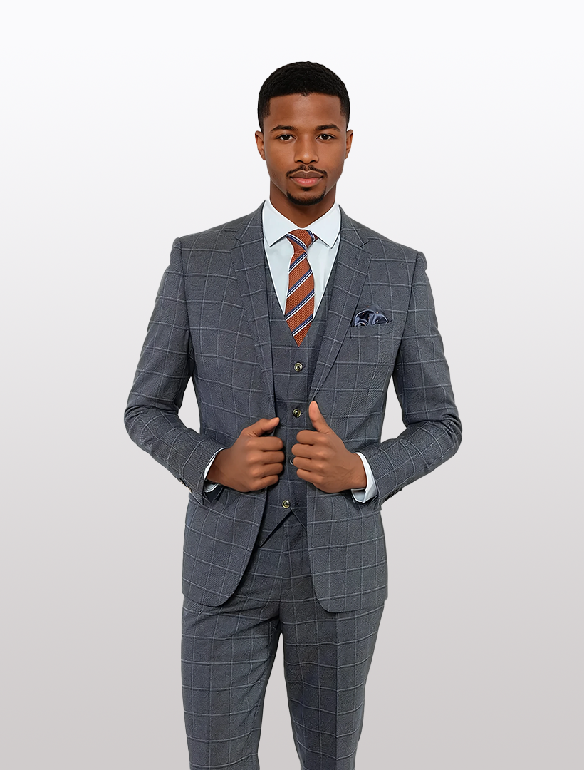 A man in a FUBU Navy Pin Check Windowpane Vested Suit by Fubu The Colle, paired with a white shirt, striped tie, and pocket square, stands against a plain light background.