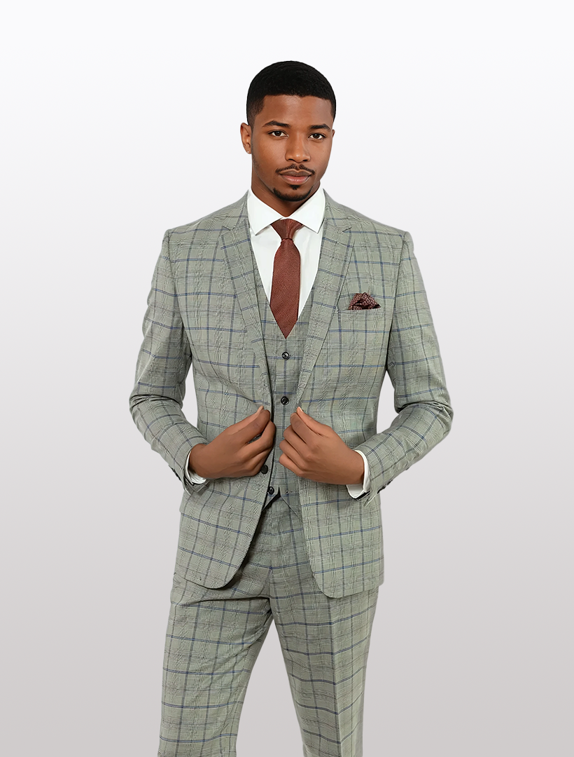 A man in a slim fit FUBU Grey with Blue Prince of Wales Check Vested Suit, complemented by a brown tie and pocket square, stands against a plain light background, showcasing modern elegance from Fubu The Colle.