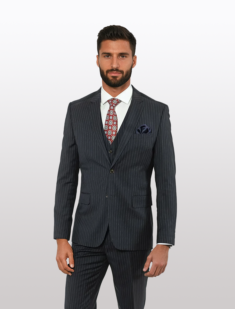 A man in a FUBU Navy with White Pinstripe Vested Suit and patterned tie stands against a plain white background, showcasing the modern elegance of the suit jacket by Fubu The Colle.