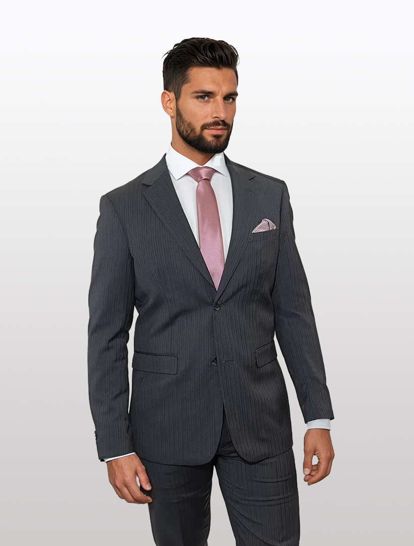 A man in the Douglas Grahame Men's Grey Chalk Stripe Wool Slim Fit Suit with a white shirt, light pink tie, and matching pocket square stands against a plain light background, showcasing modern prom style.