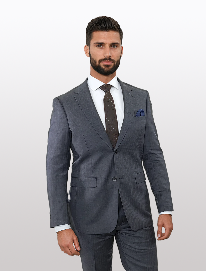 A bearded man, elegantly dressed in a Douglas Grahame Men's Grey Double Stripe Wool Slim Fit Suit with a white shirt and polka dot tie, stands against a plain background.