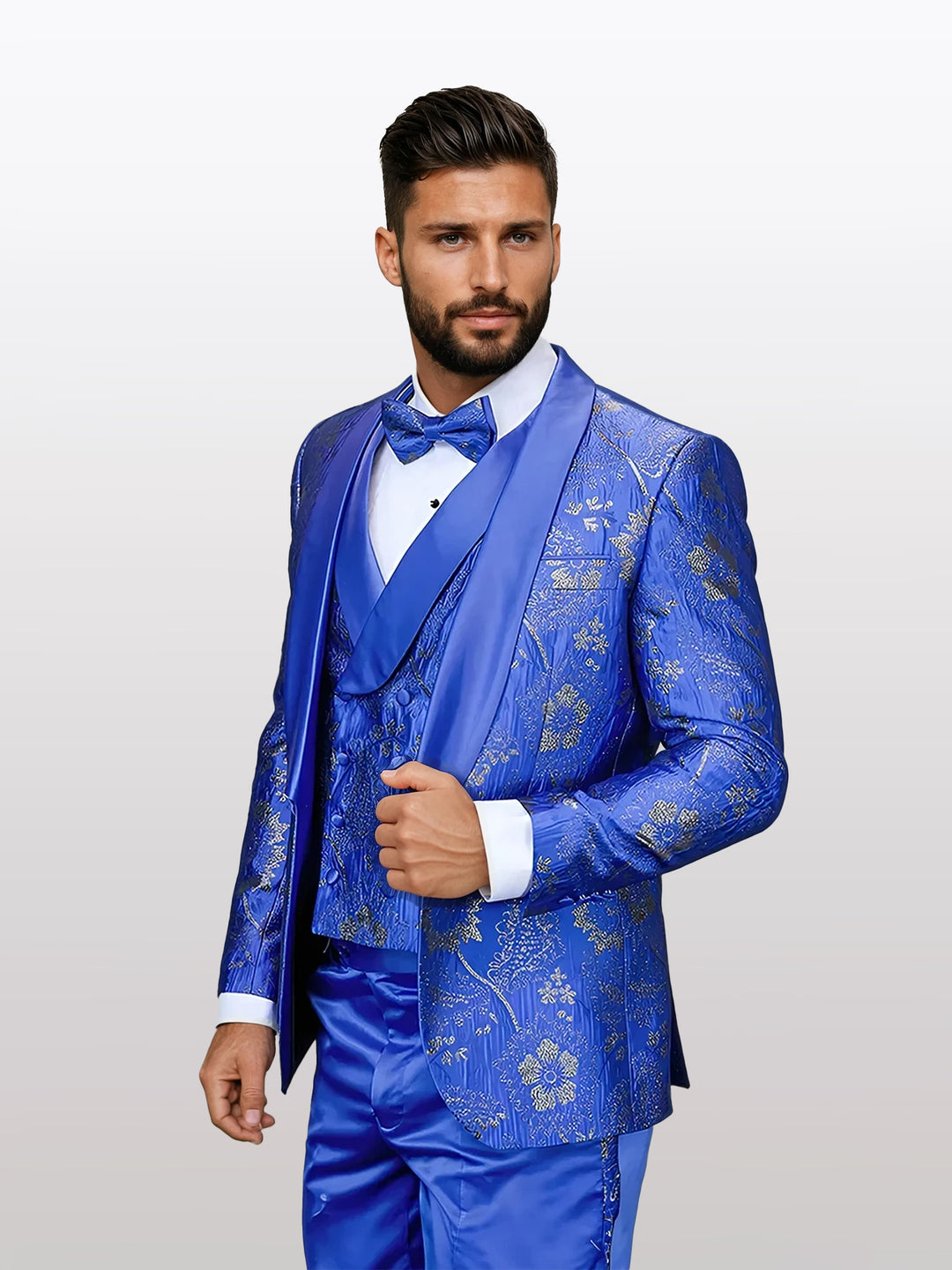 Dressed in the Statement Men's Royal Blue Patterned Vested Tuxedo with Bowtie, crafted from 100% wool, a man showcases elegance in a vibrant blue suit adorned with gold floral patterns and paired with a matching vest and bow tie against a neutral background.
