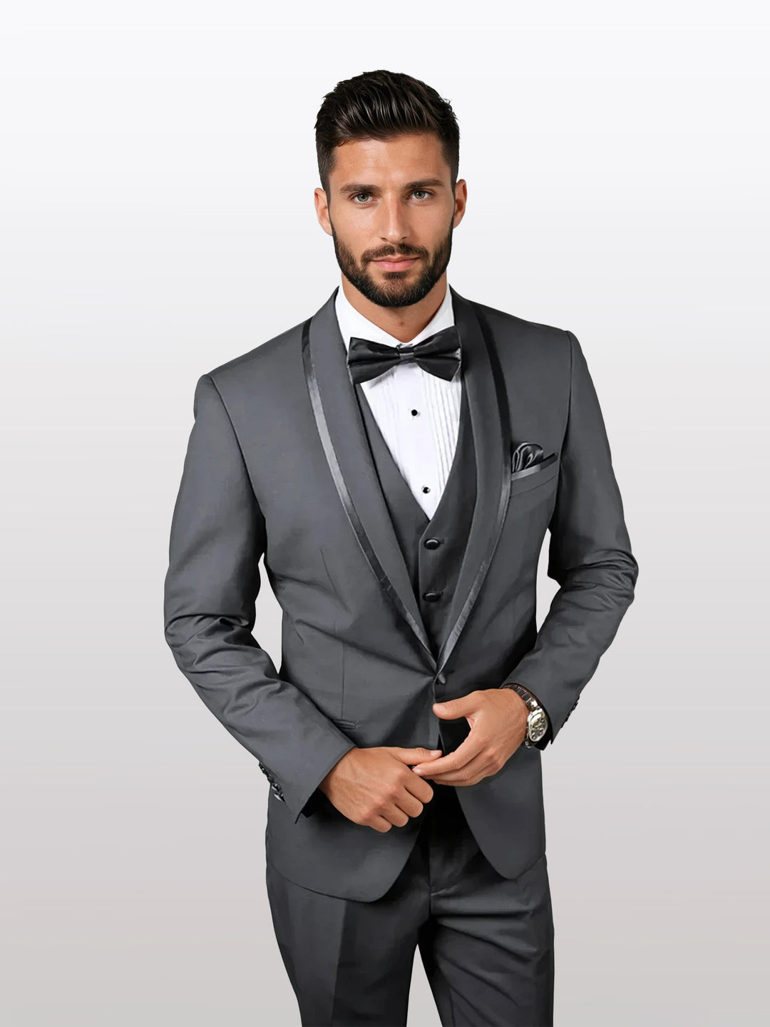 A man models the Statement Men's Charcoal Vested Tuxedo with Shawl Lapel and Bowtie, featuring a tailored fit from 100% wool. He wears it with a black bow tie and crisp white shirt against a plain background.
