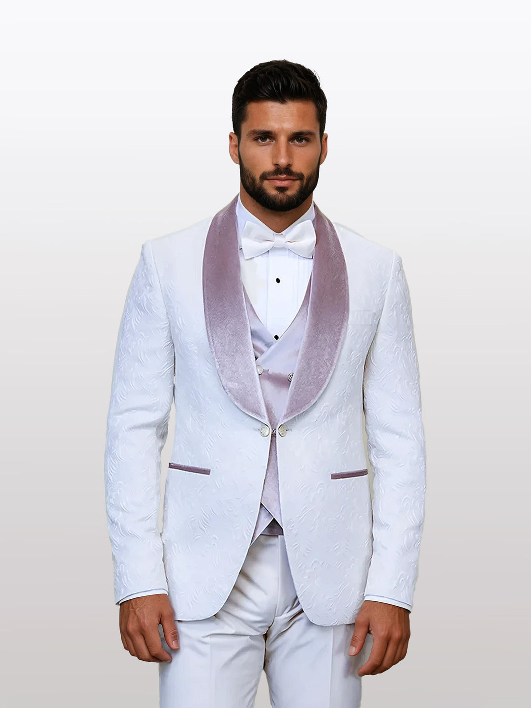 A man models the Statement Men's Ivory Velvet Shawl Lapel Tuxedo with a velvet vest, standing against a plain backdrop and featuring a light purple velvet lapel and bow tie.