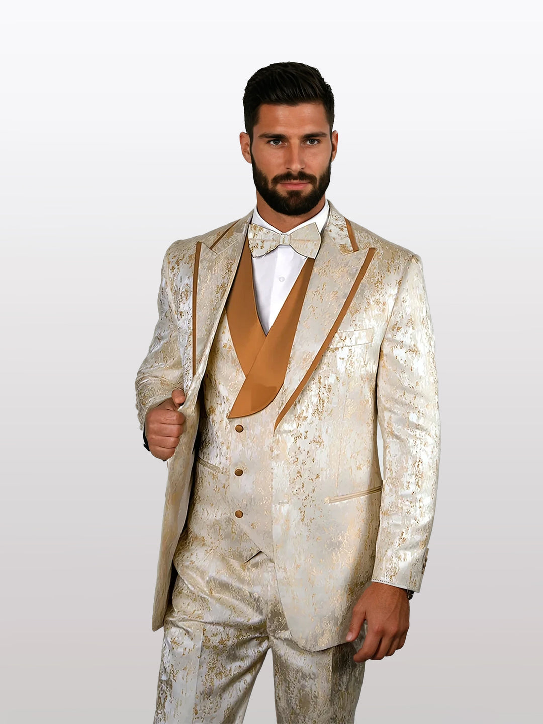 A man poses against a plain background wearing the Statement Men's Gold Jacquard Vested Tuxedo with Pleated Pants, complete with a matching vest and bow tie.