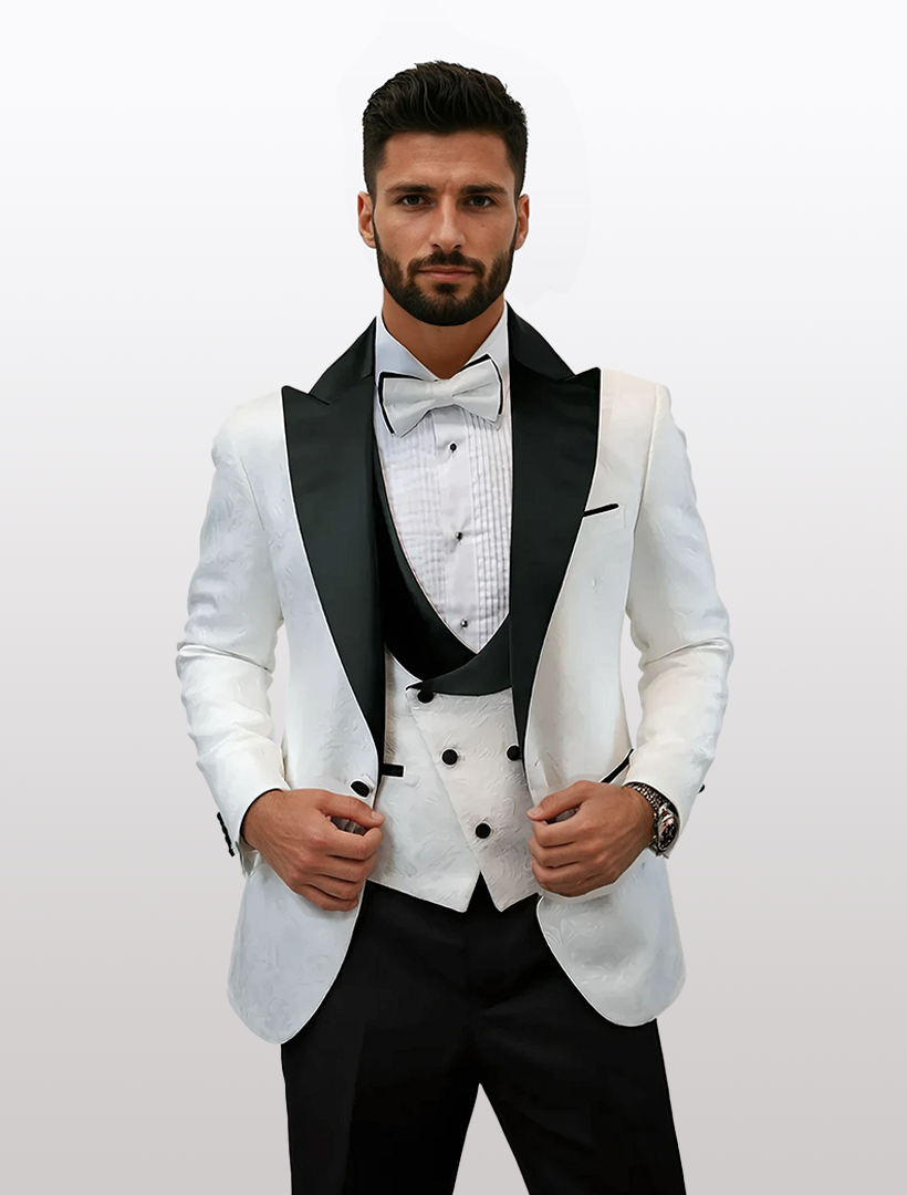 A man in a modern Statement Men's White Tuxedo, featuring black peak lapels and a bow tie, stands against a plain background.