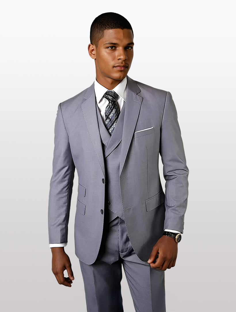 A man stands elegantly in a Statement Mens Grey Modern Fit 100% Wool Vested Suit, featuring a white shirt, patterned tie, and double-breasted vest against a plain background.